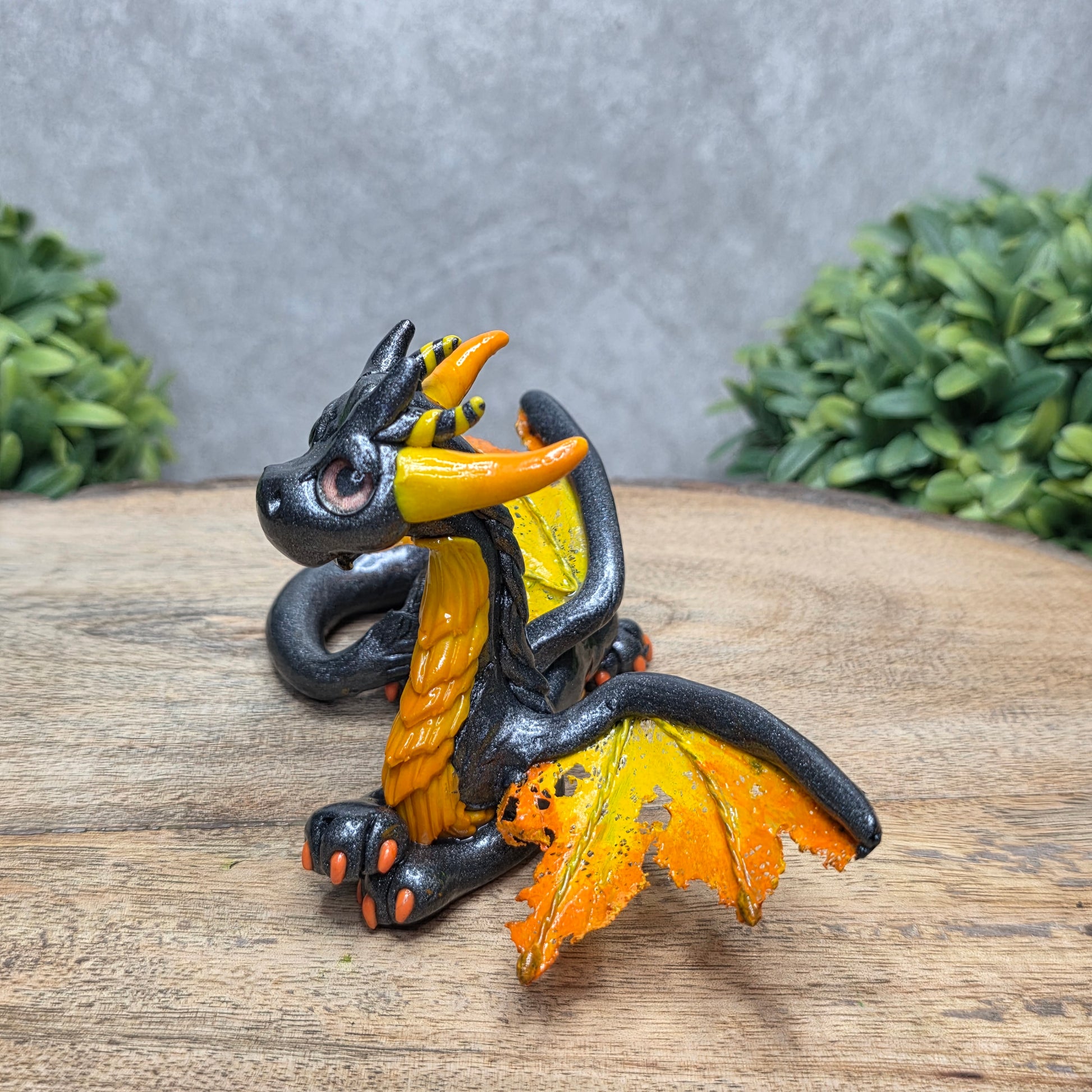 Side view of a clay dragon against a wood surface with greenery.