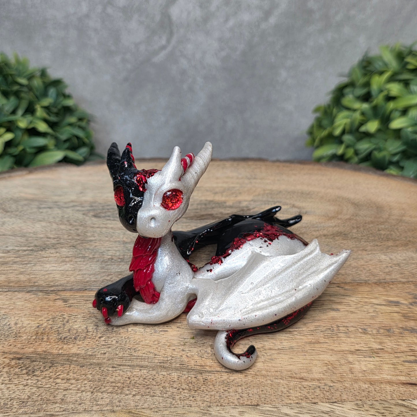 A 2 toned clay dragon sculpture on a wood surface with greenery.