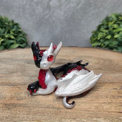 A 2 toned clay dragon sculpture on a wood surface with greenery.