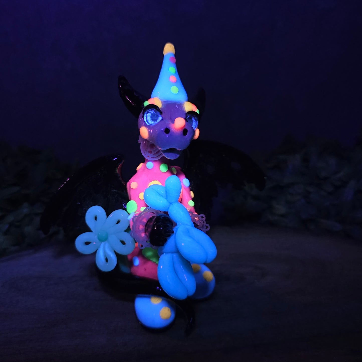 A blacklight reactive clown dragon with balloon animals on wood surface with greenery