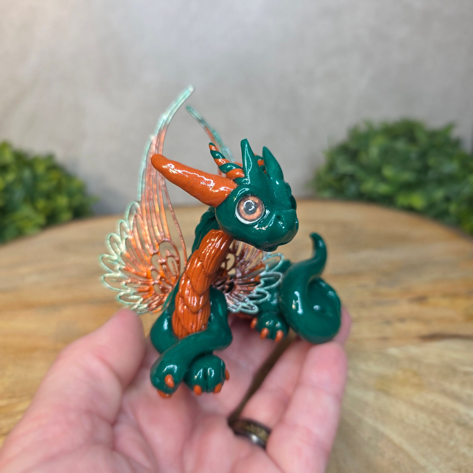 Hand holding a small green and orange dragon figurine with a blurred background