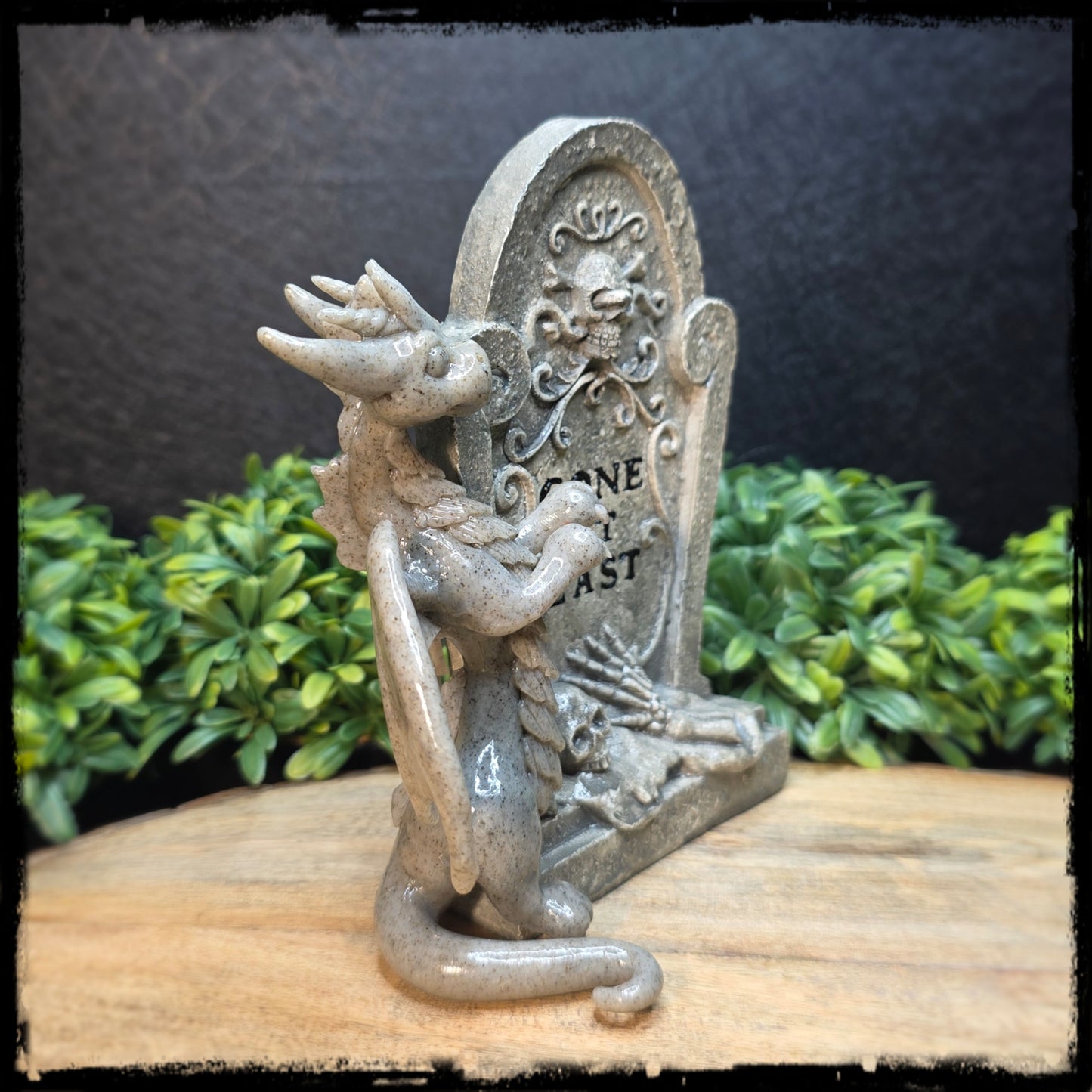 Statue of a winged dragon with a tombstone with a green foliage background