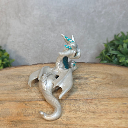 A white and teal clay dragon against a blurred wood surface