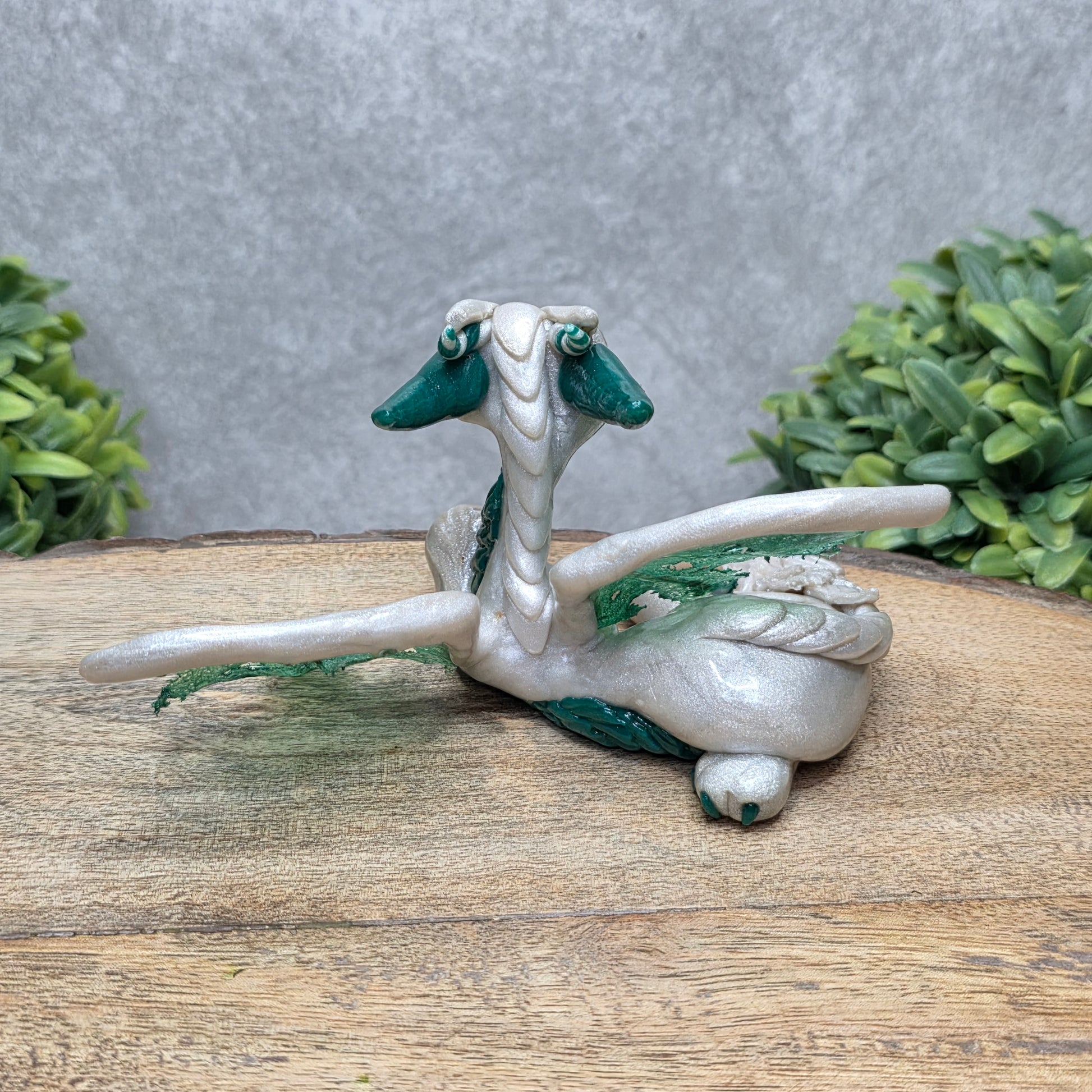Back view of a clay dragon against a wood surface with greenery.
