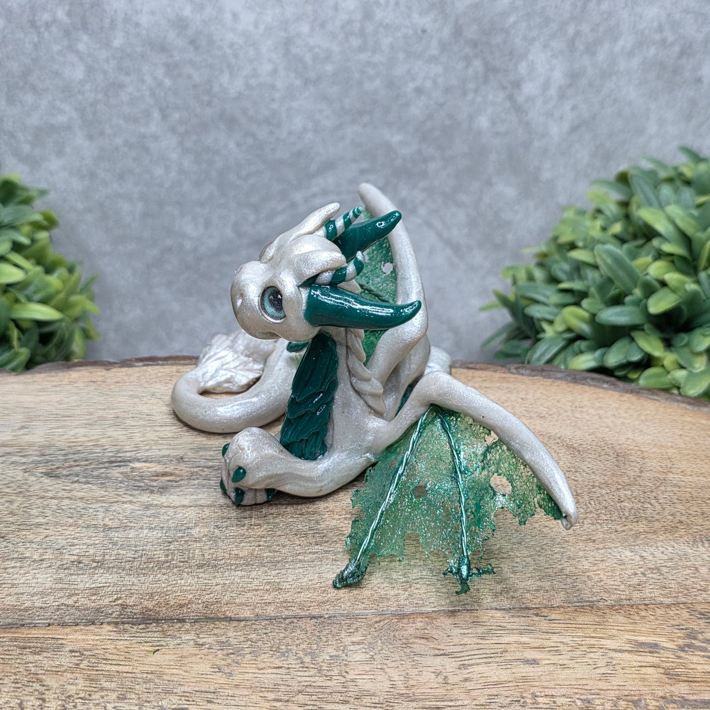 Side view of a clay dragon against a wood surface with greenery.
