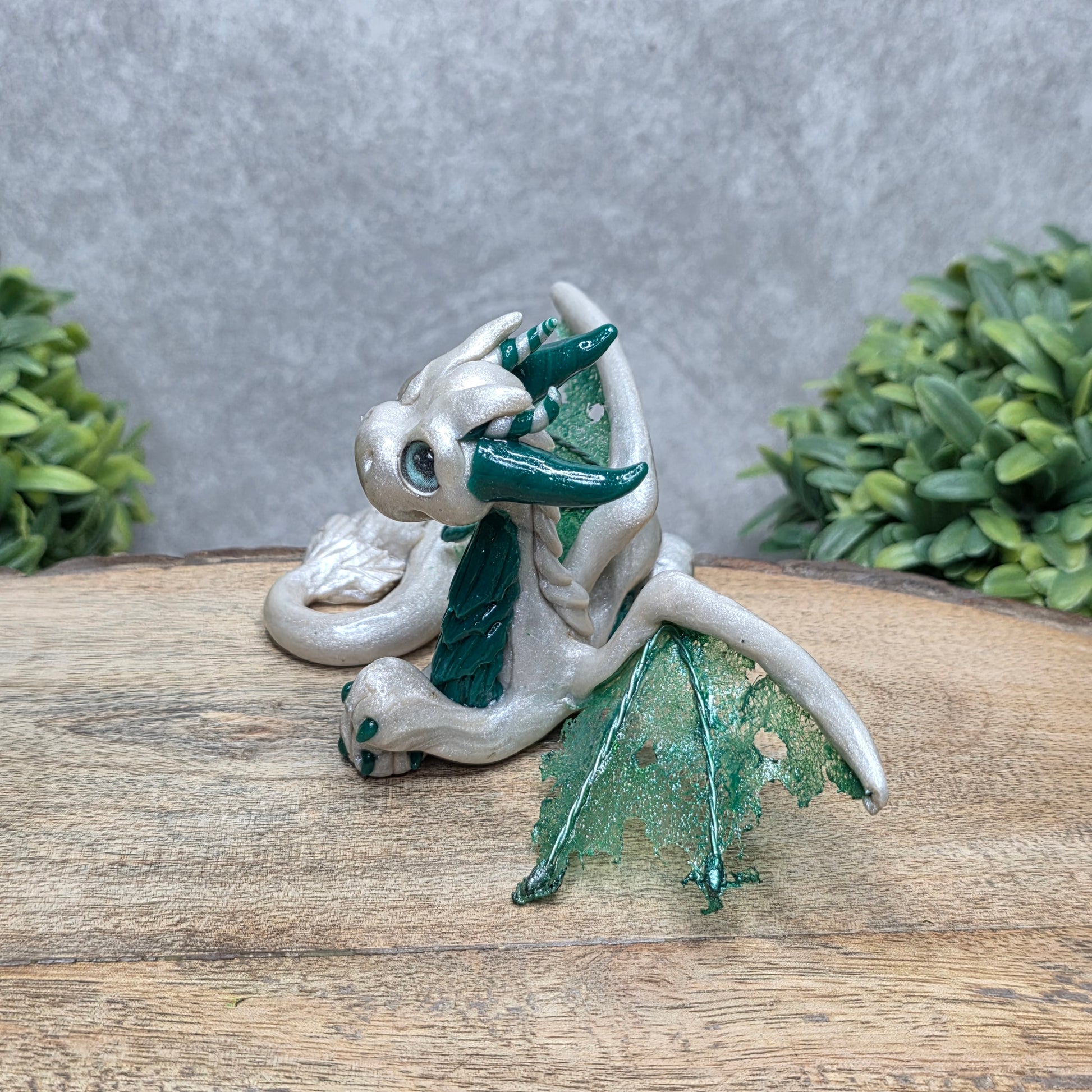 Side view of a clay dragon against a wood surface with greenery.