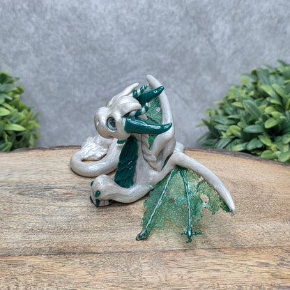 Side view of a clay dragon against a wood surface with greenery.