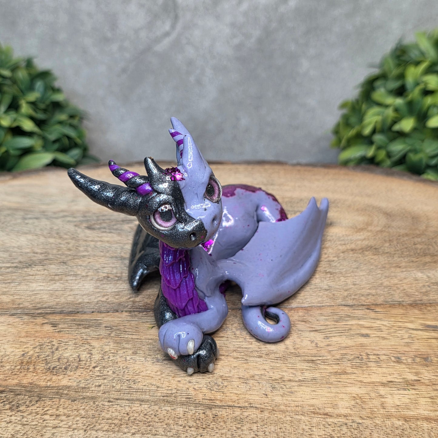 A 2 toned clay dragon sculpture on a wood surface with greenery.