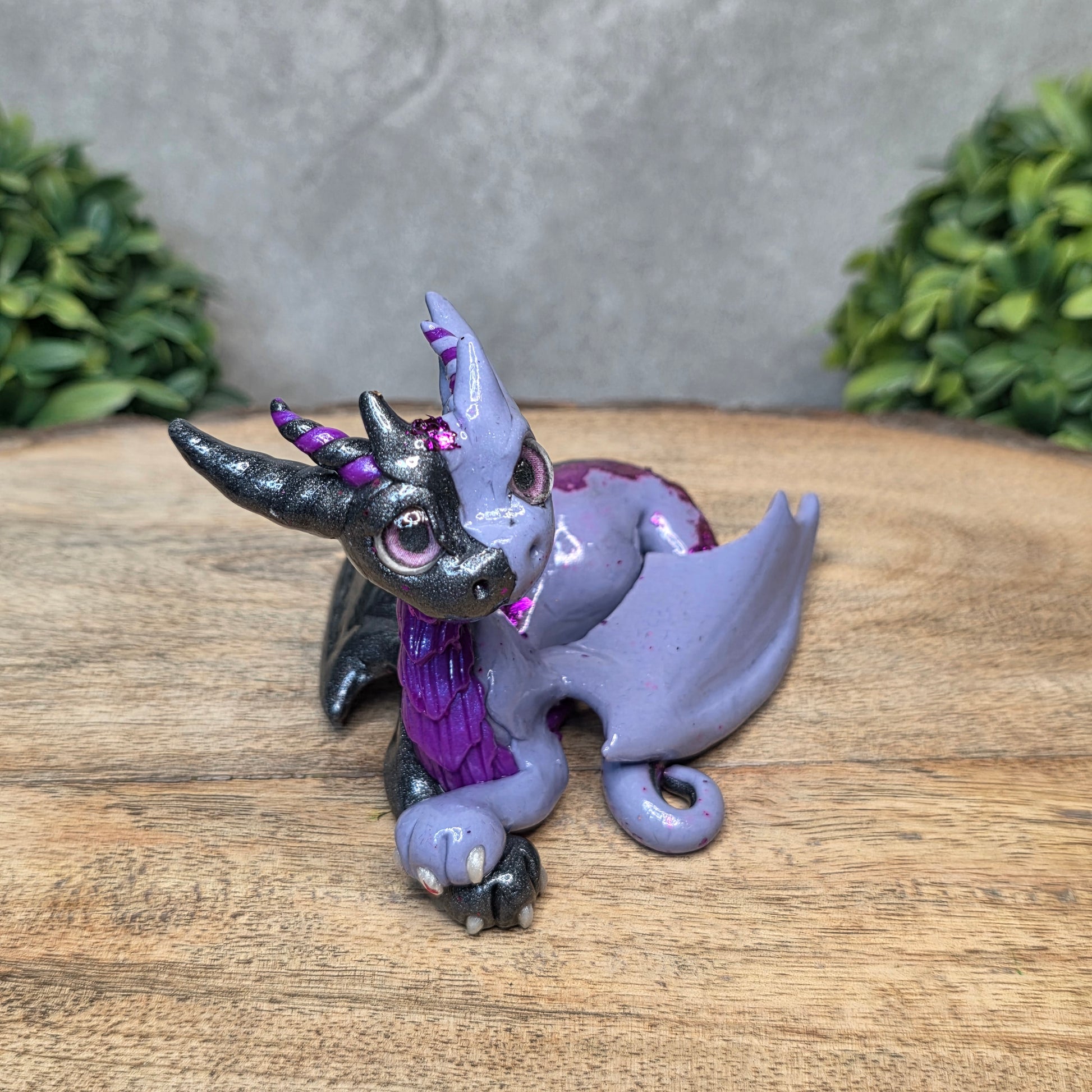 A 2 toned clay dragon sculpture on a wood surface with greenery.