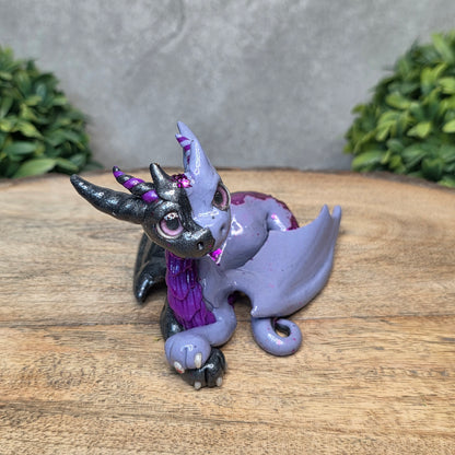 A 2 toned clay dragon sculpture on a wood surface with greenery.