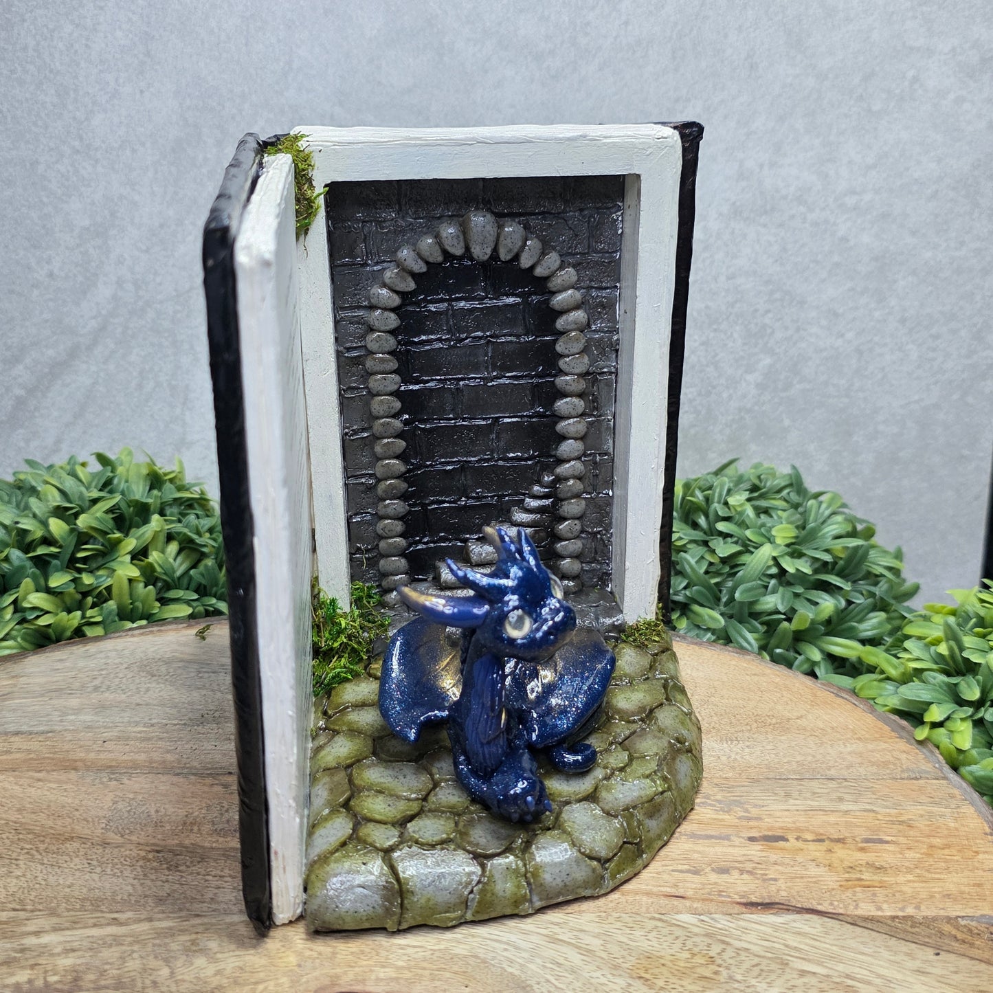 Book nook with dragon on a wood surface with greenery