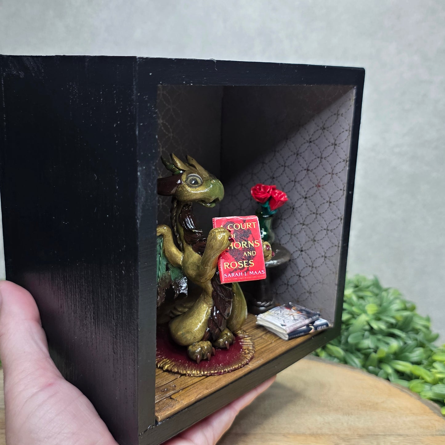 Book nook with dragon on a wood surface with greenery