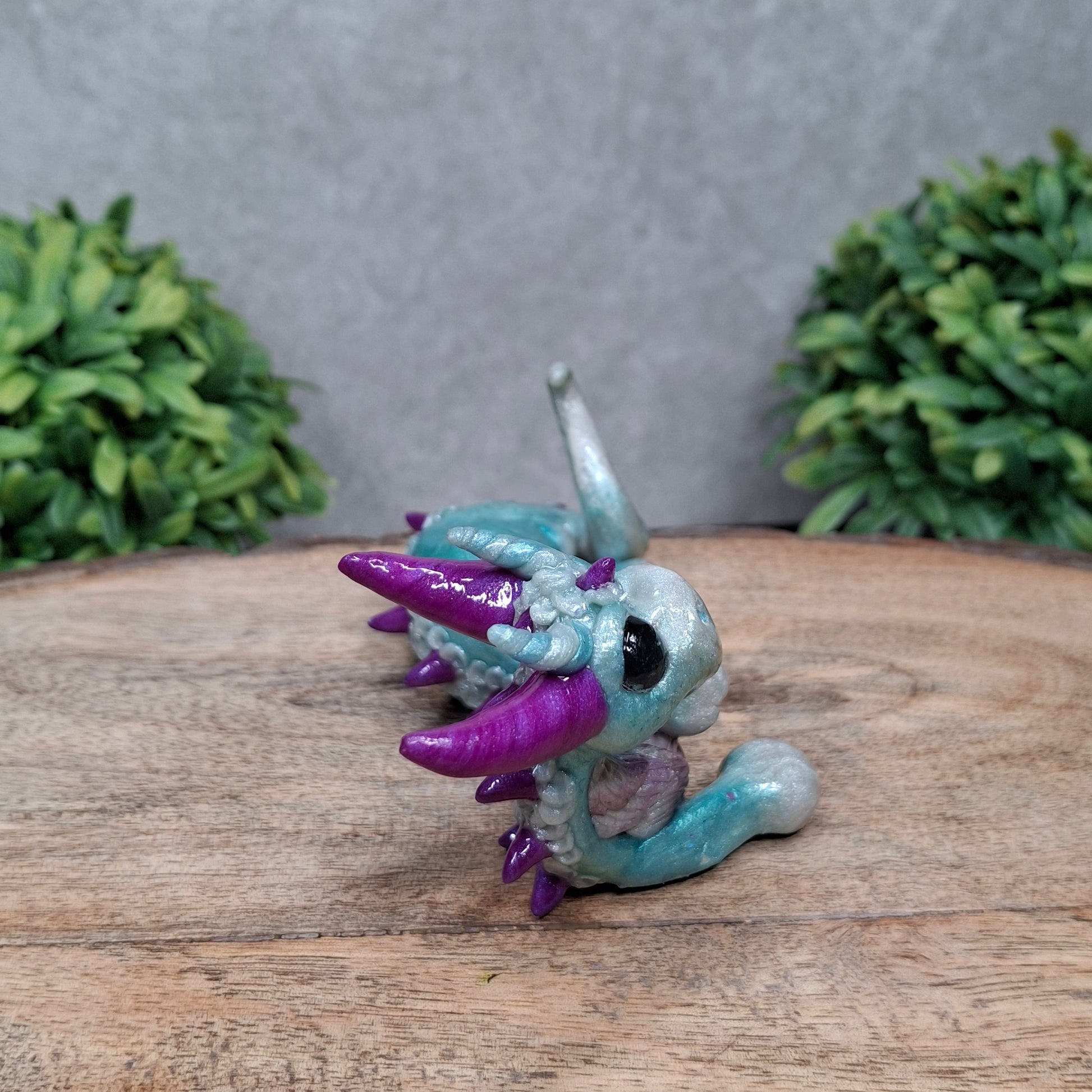 A clay dragon against a wood background with greenery