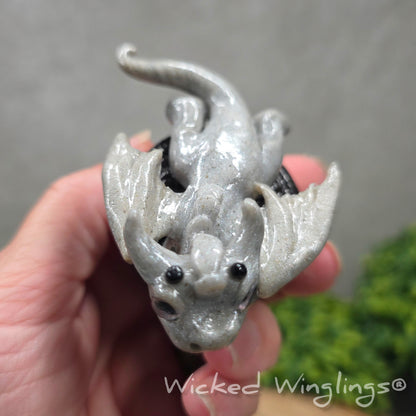 Top view of a hand holding a baby clay dragon with a cookie with a Wicked Winglings® watermark.
