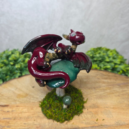 Small dragon figurine on a wooden surface with greenery
