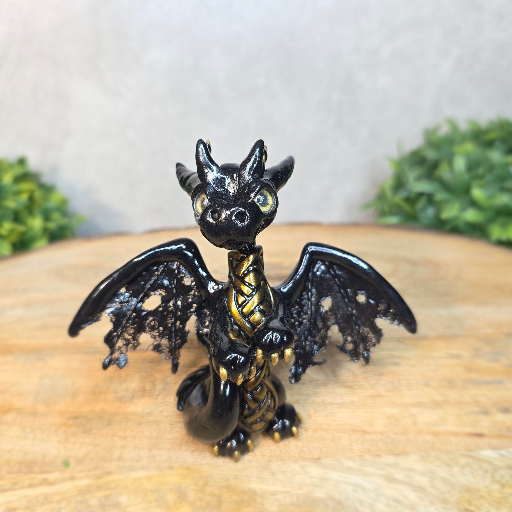 A clay dragon figurine on a wooden surface with a blurred green plant in the background