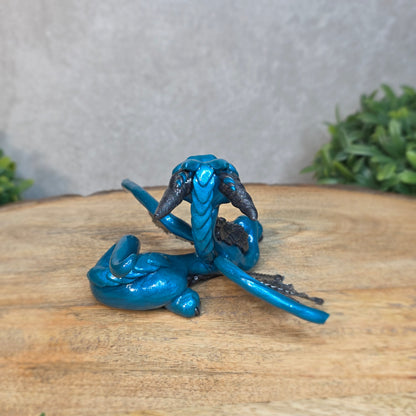 A blue and graphite clay dragon against a blurred wood surface