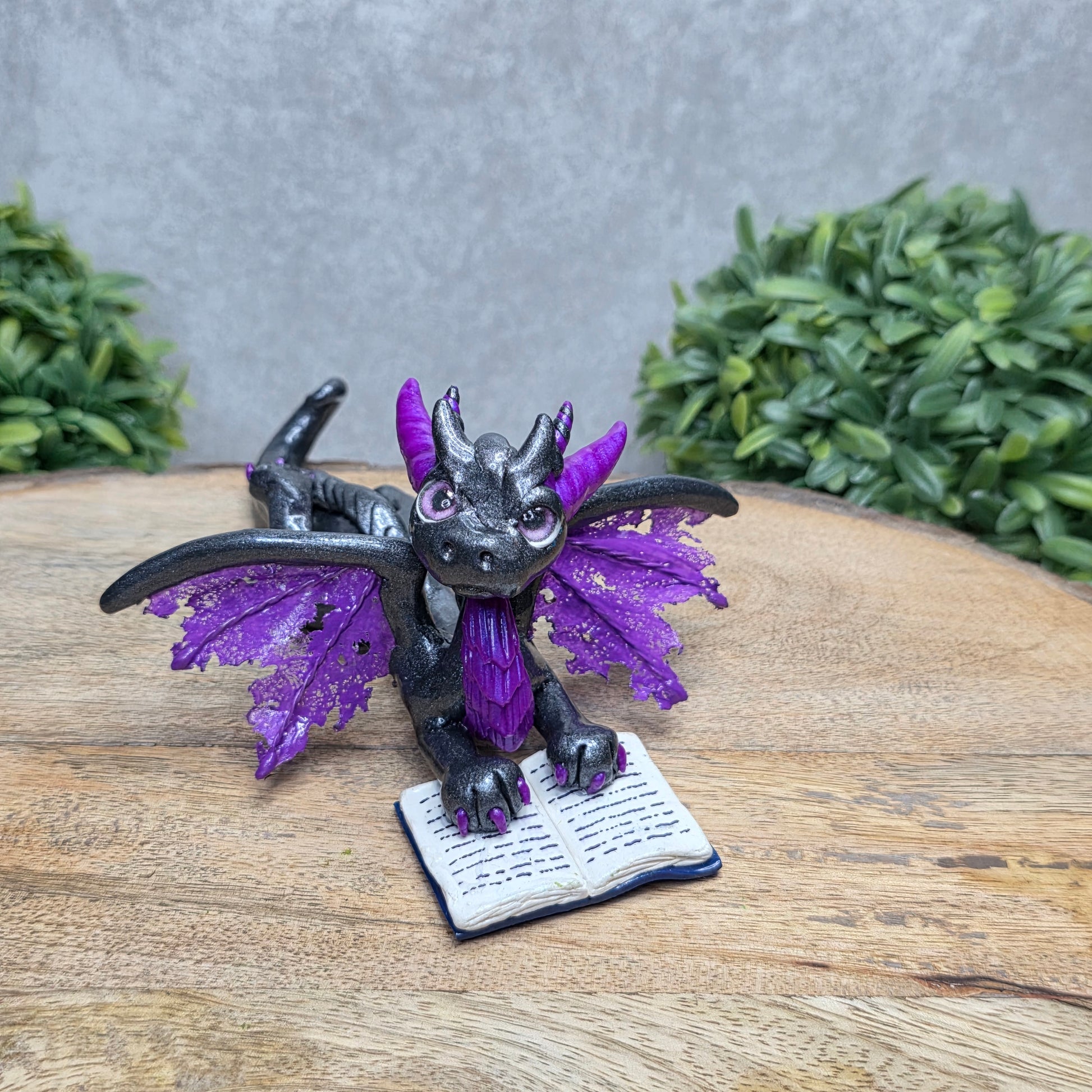 A dragon reading a book against a wood surface with greenery