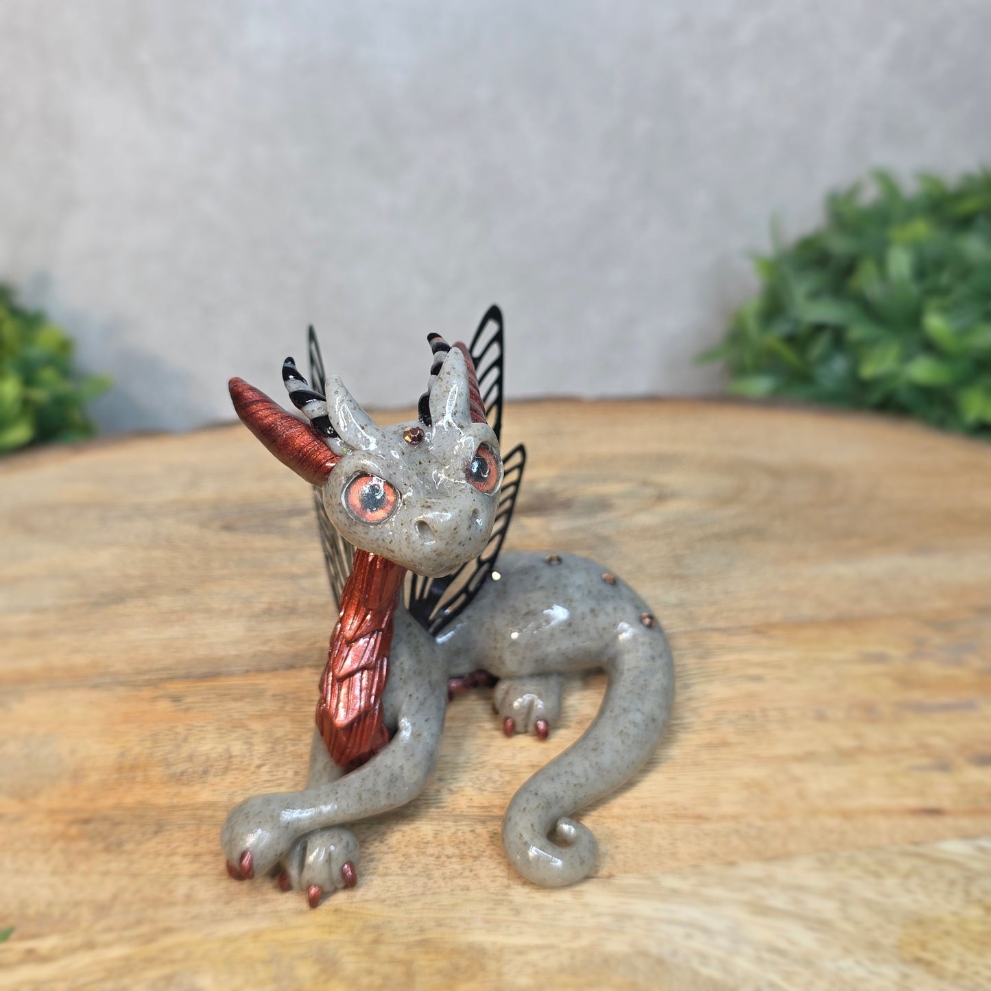 Decorative dragon figurine on a wooden surface with a blurred green plant in the background