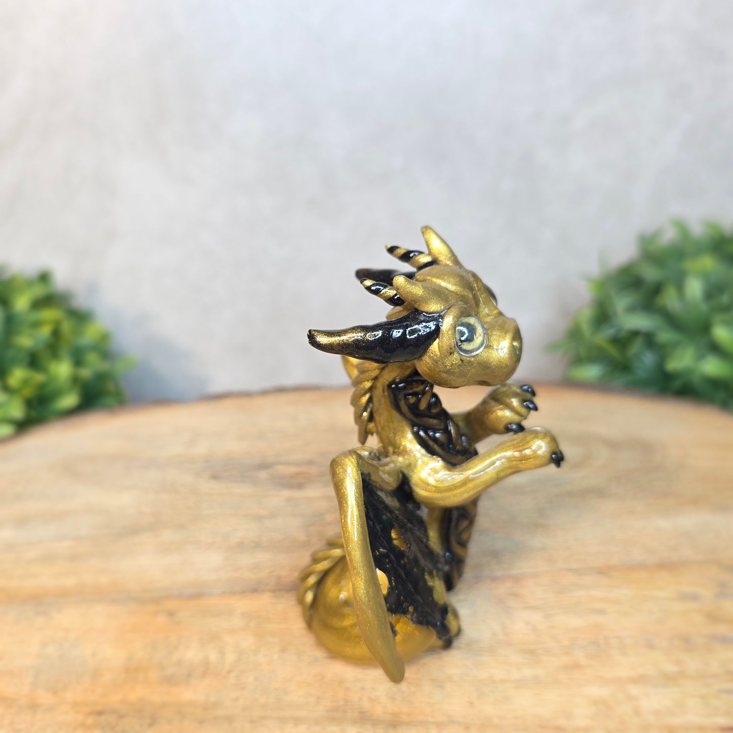 A clay dragon figurine on a wooden surface with a blurred green plant in the background