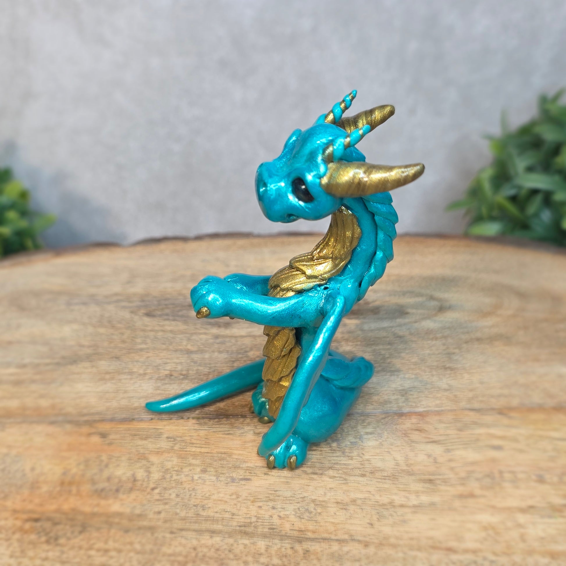 A teal and gold clay dragon against a blurred wood surface