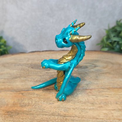 A teal and gold clay dragon against a blurred wood surface