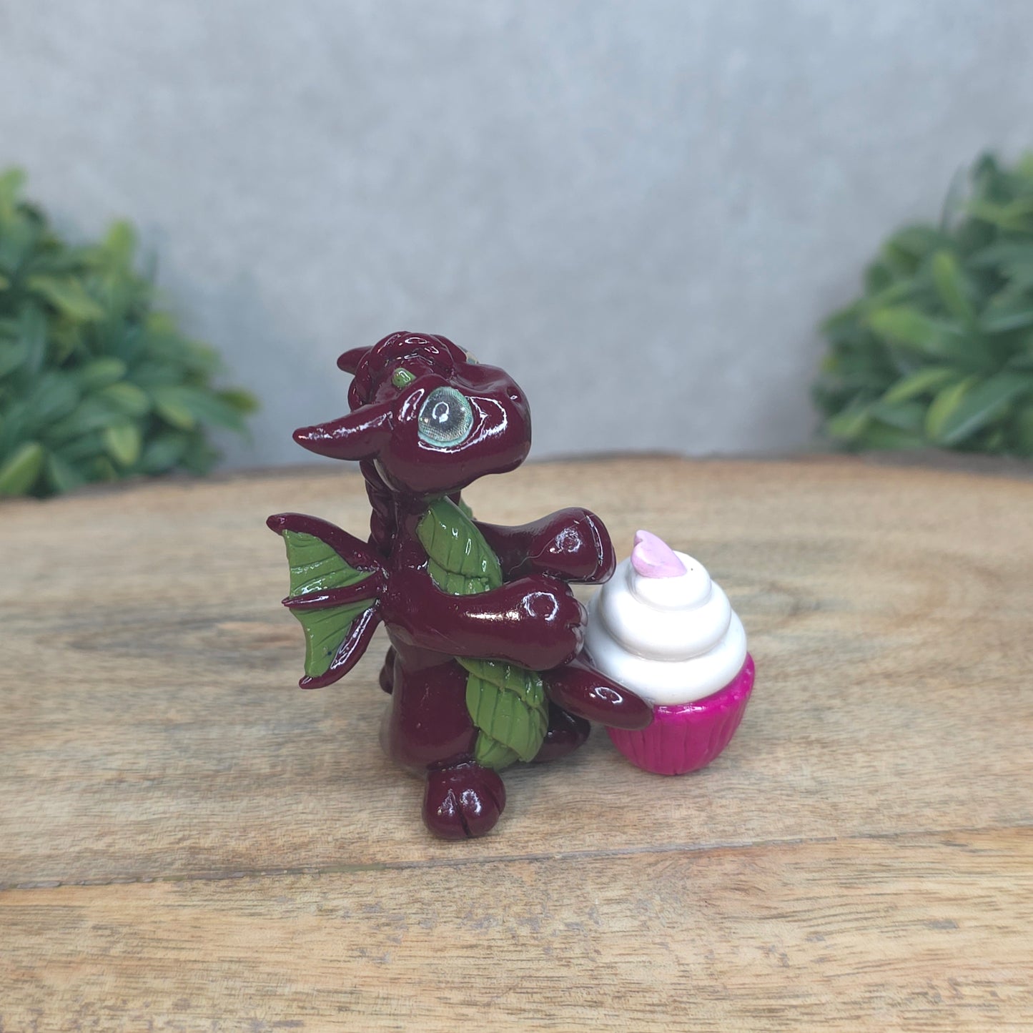 A baby polymer clay dragon with a cupcake against a blurred background