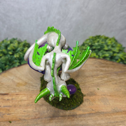 A clay dragon figurine on a  mushroom on a wooden surface with greenery.
