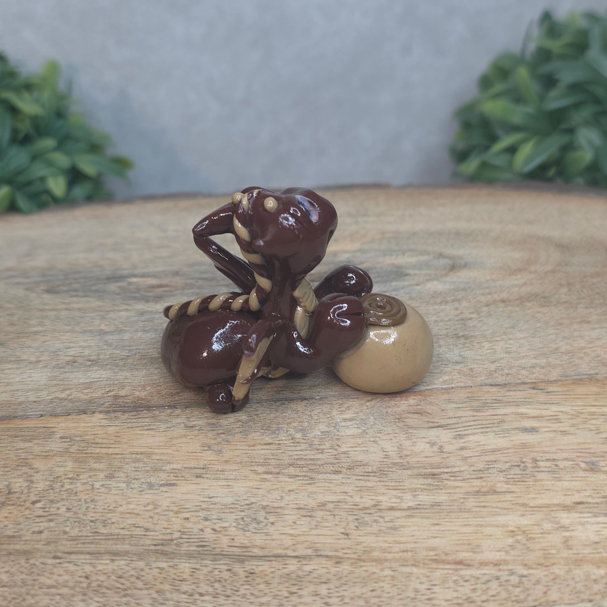 A baby polymer clay dragon with a chocolate truffle against a blurred background
