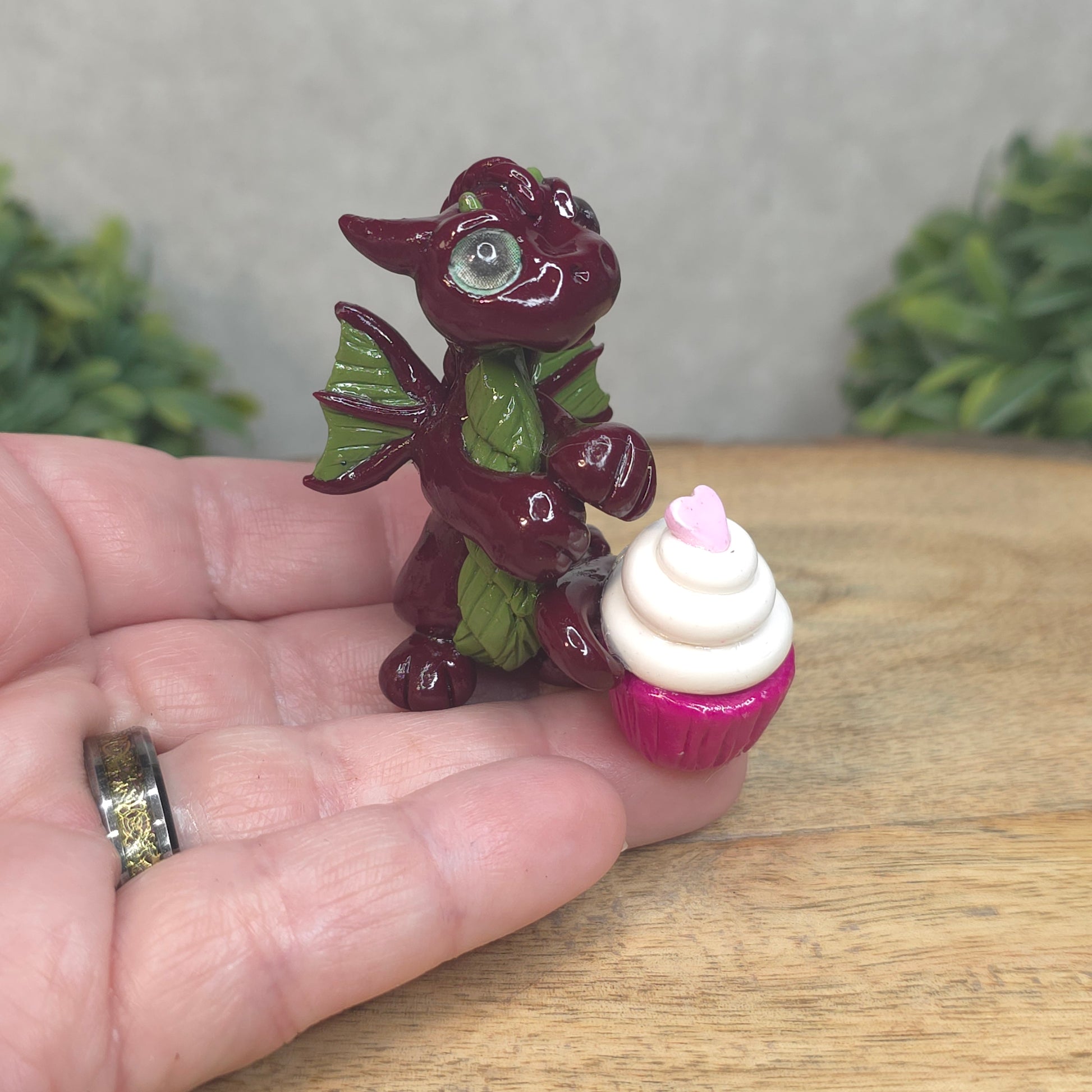 A hand holding a baby polymer clay dragon with a cupcake  against a blurred background