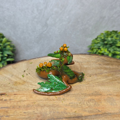 A clay dragon accented with moss and mushrooms against a wood surface with greenery.