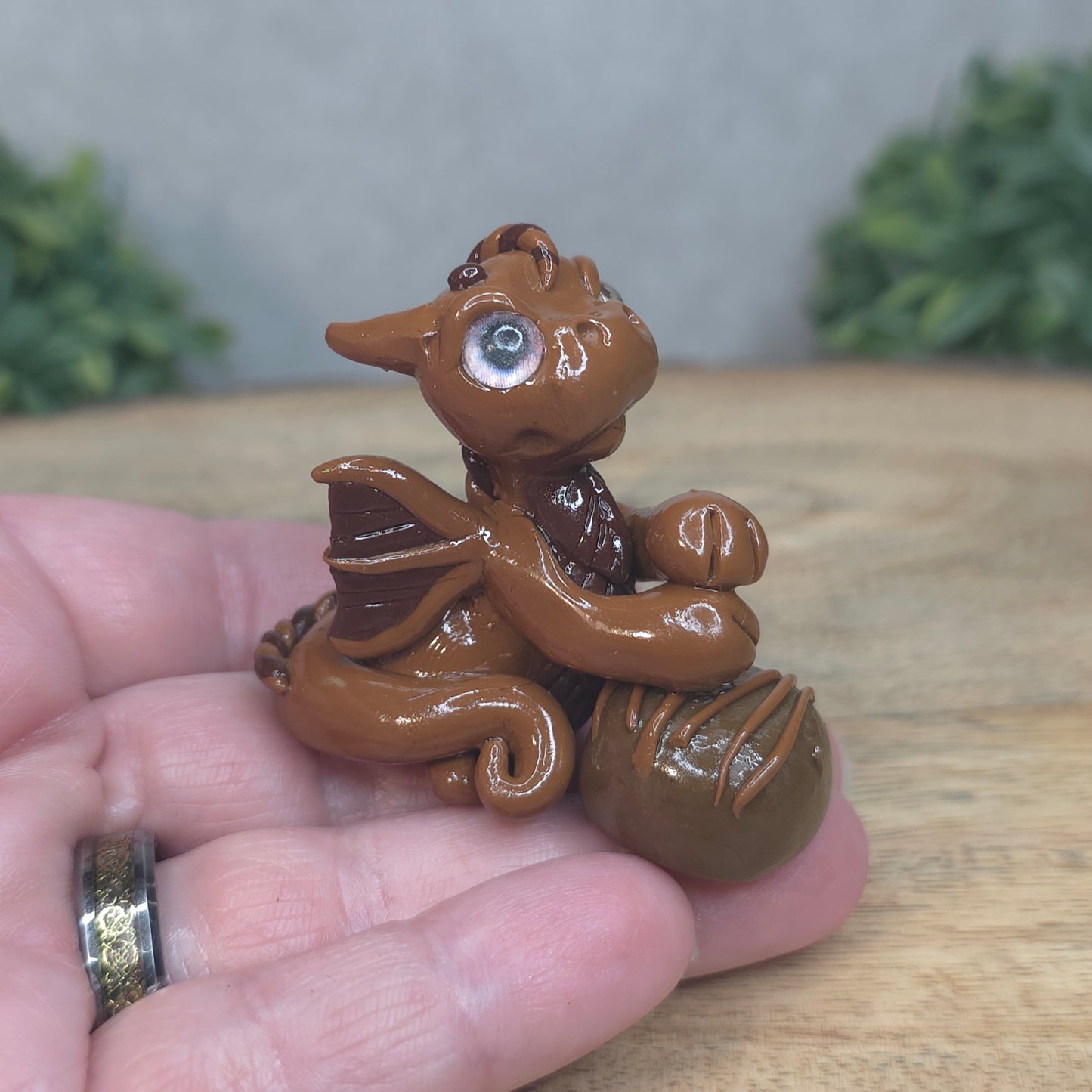A hand holding a baby polymer clay dragon with a chocolate truffle against a blurred background