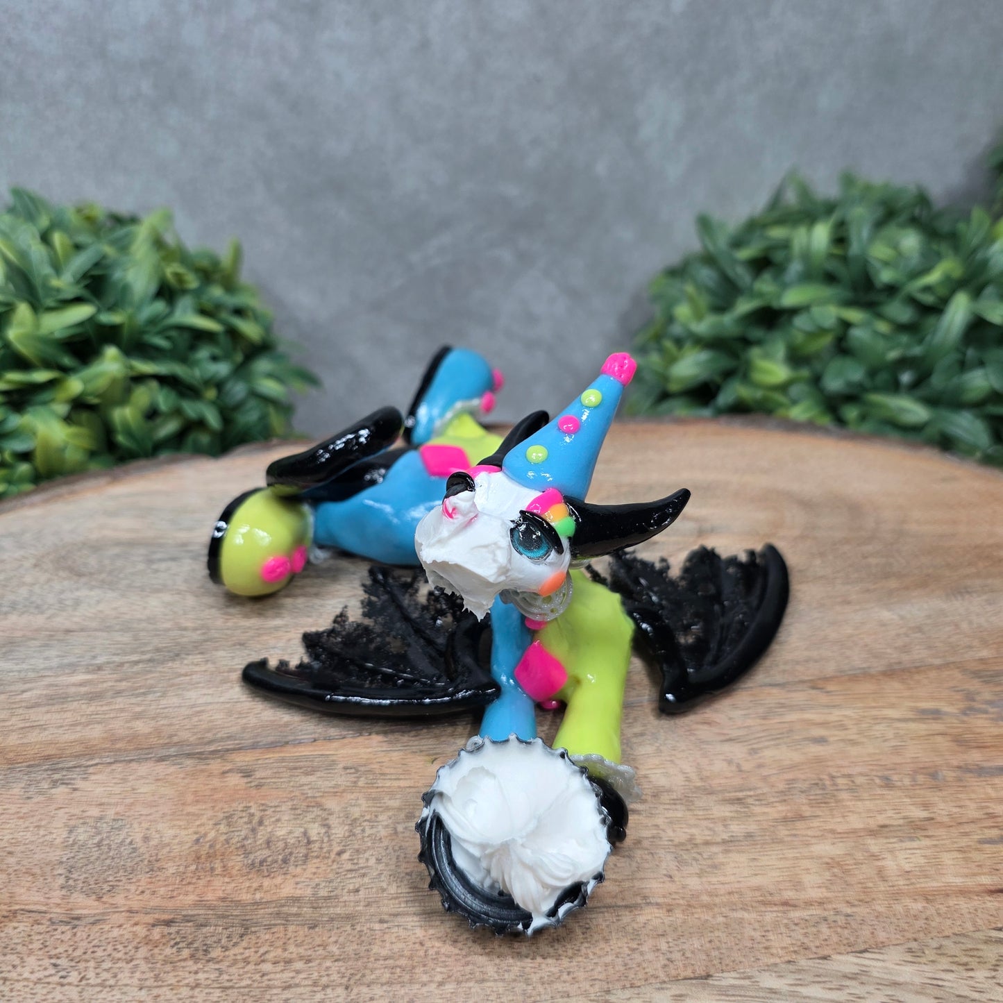 A clown dragon with cream pie on face on wood surface with greenery