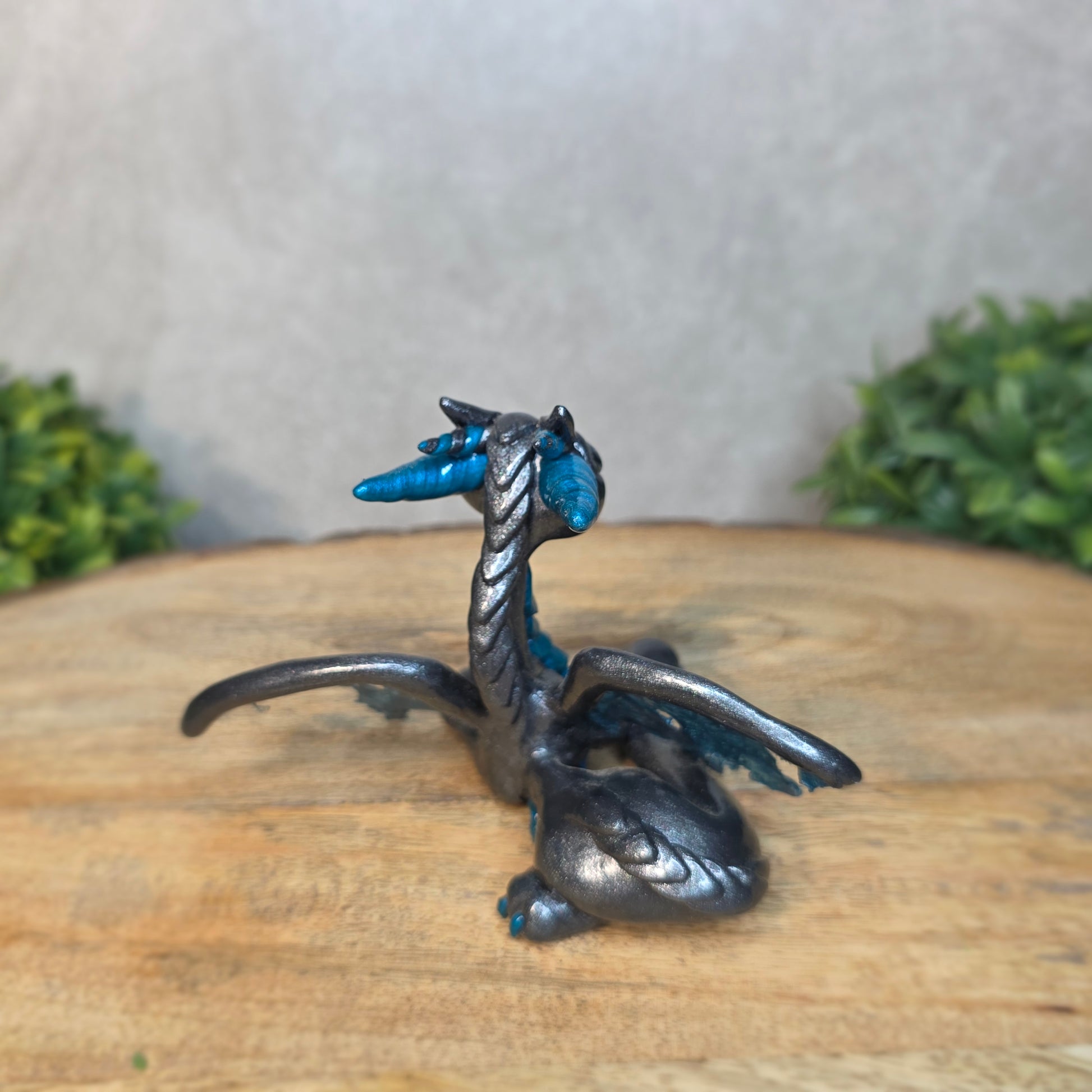 A graphite and blue clay dragon against a blurred wood surface