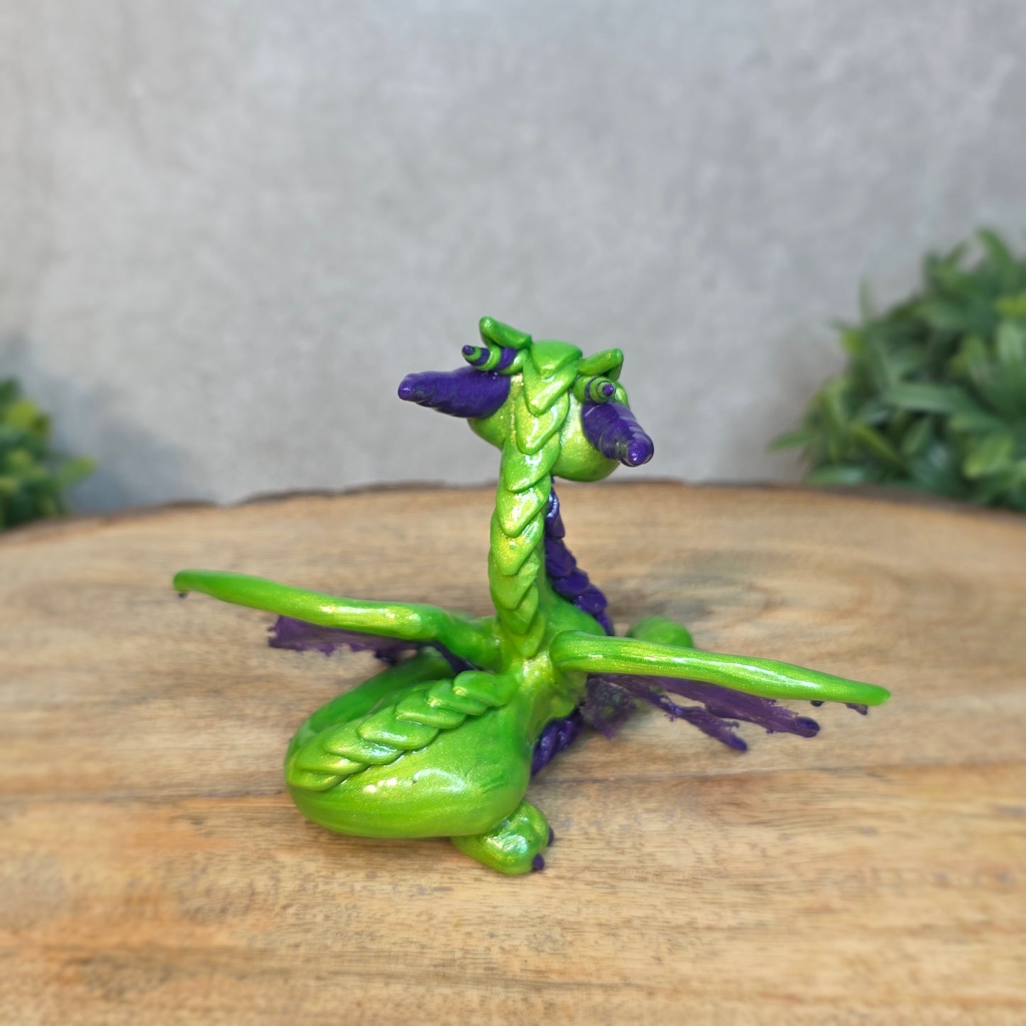 A green and purple clay dragon against a blurred wood surface