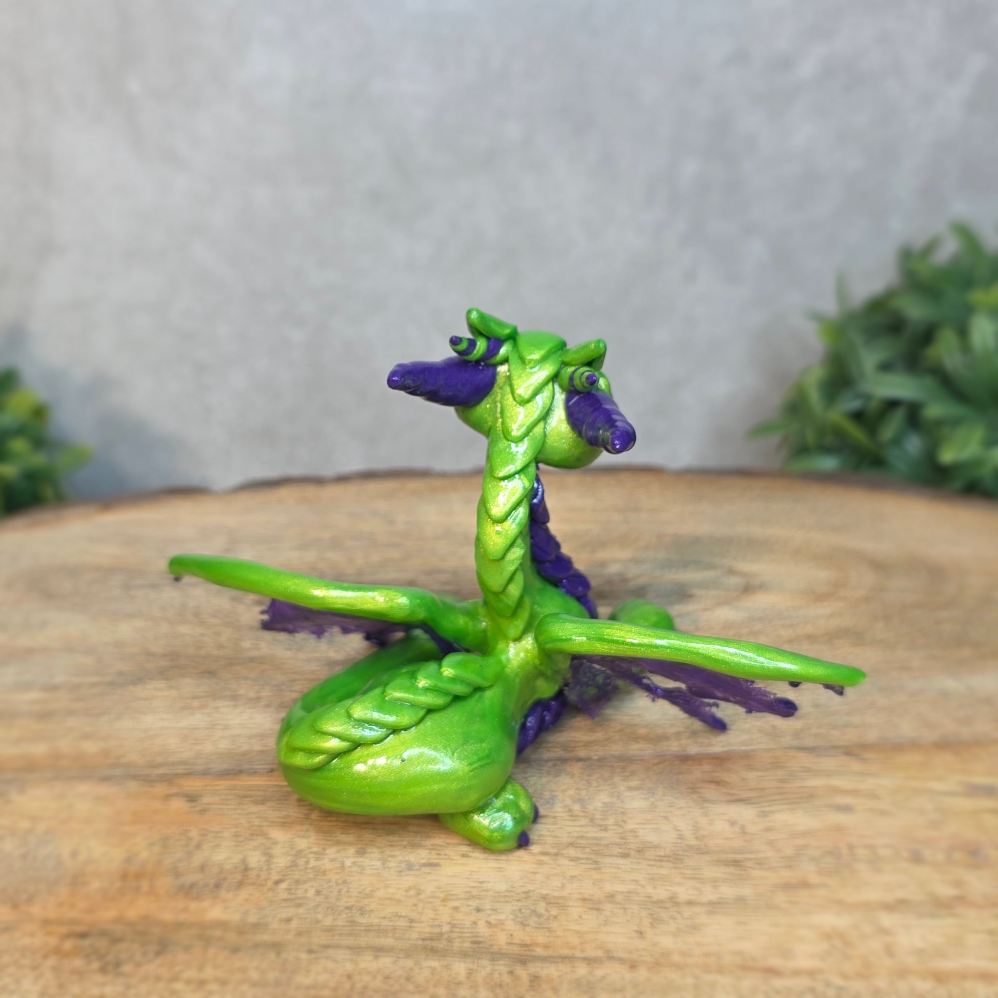 A green and purple clay dragon against a blurred wood surface
