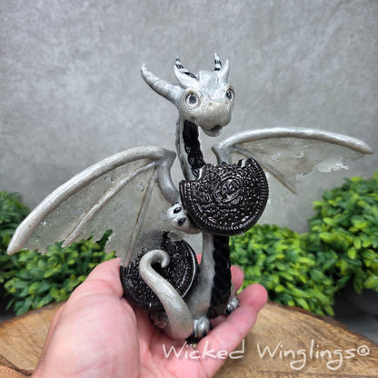 A hand holding a  large clay dragon with cookies with a Wicked Winglings® watermark.