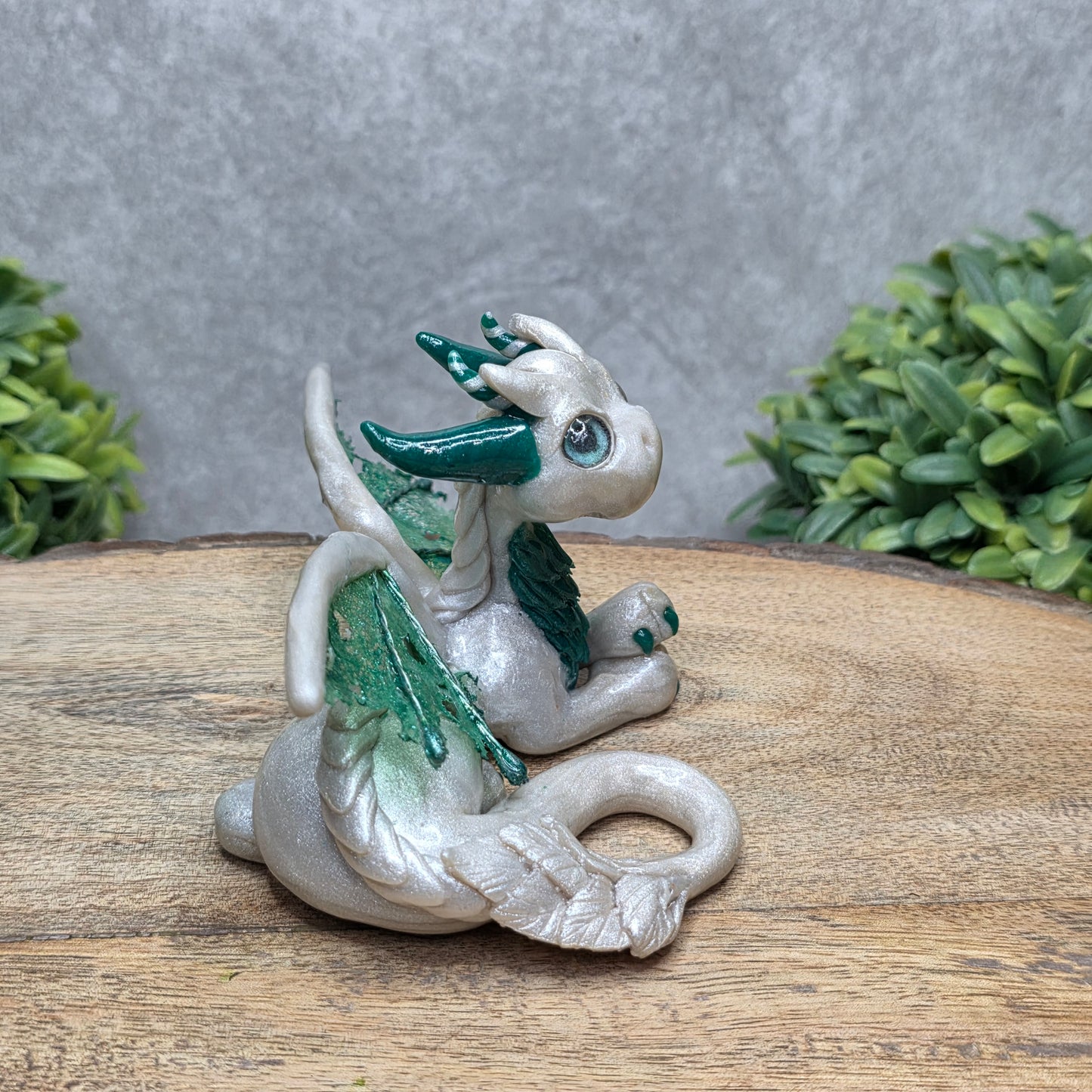 Side view of a clay dragon against a wood surface with greenery.