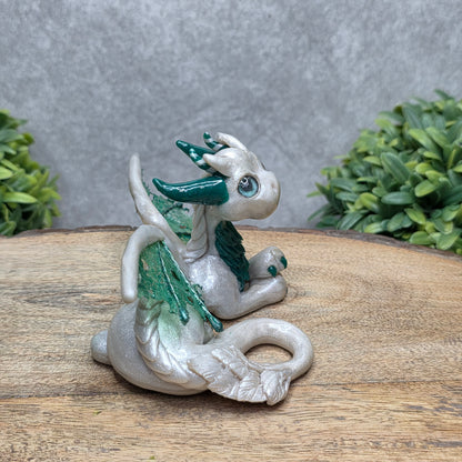 Side view of a clay dragon against a wood surface with greenery.