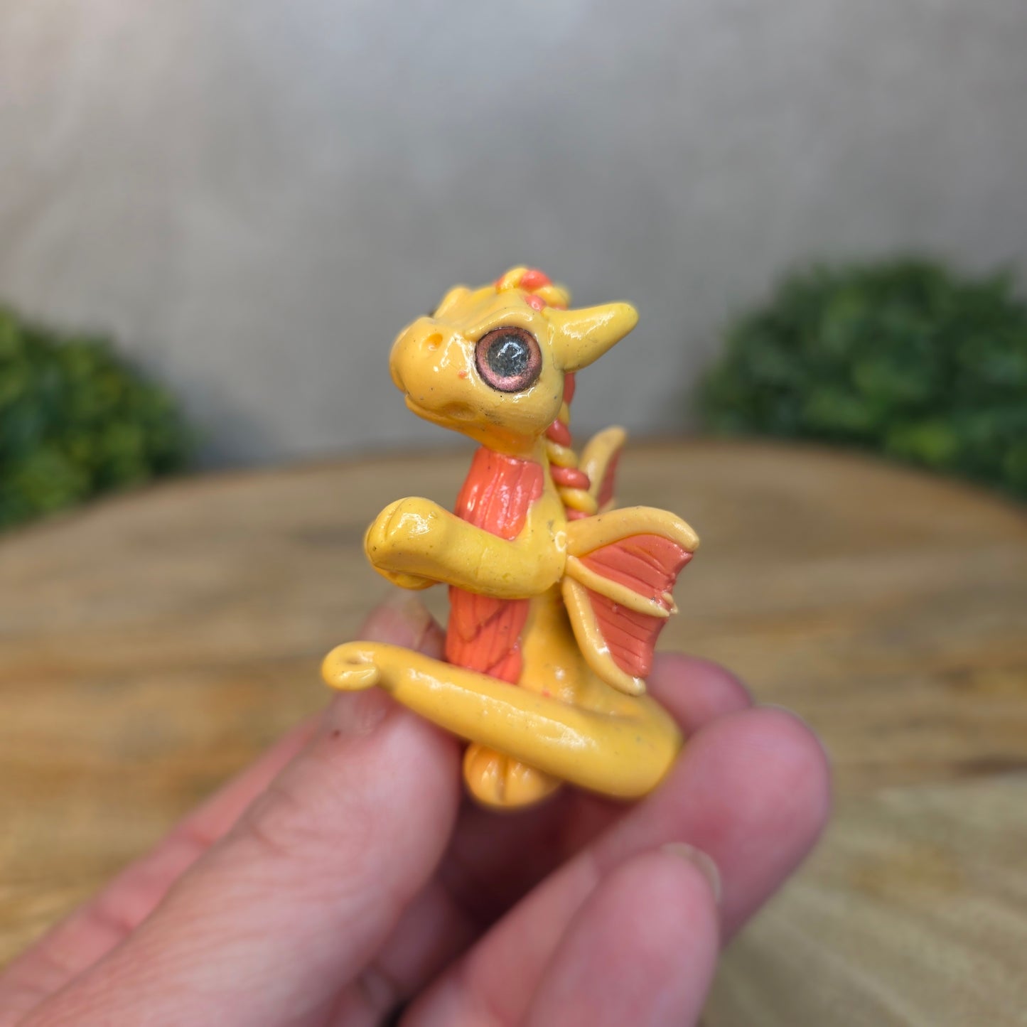 A hand holding a small peach dragon against a blurred wood background