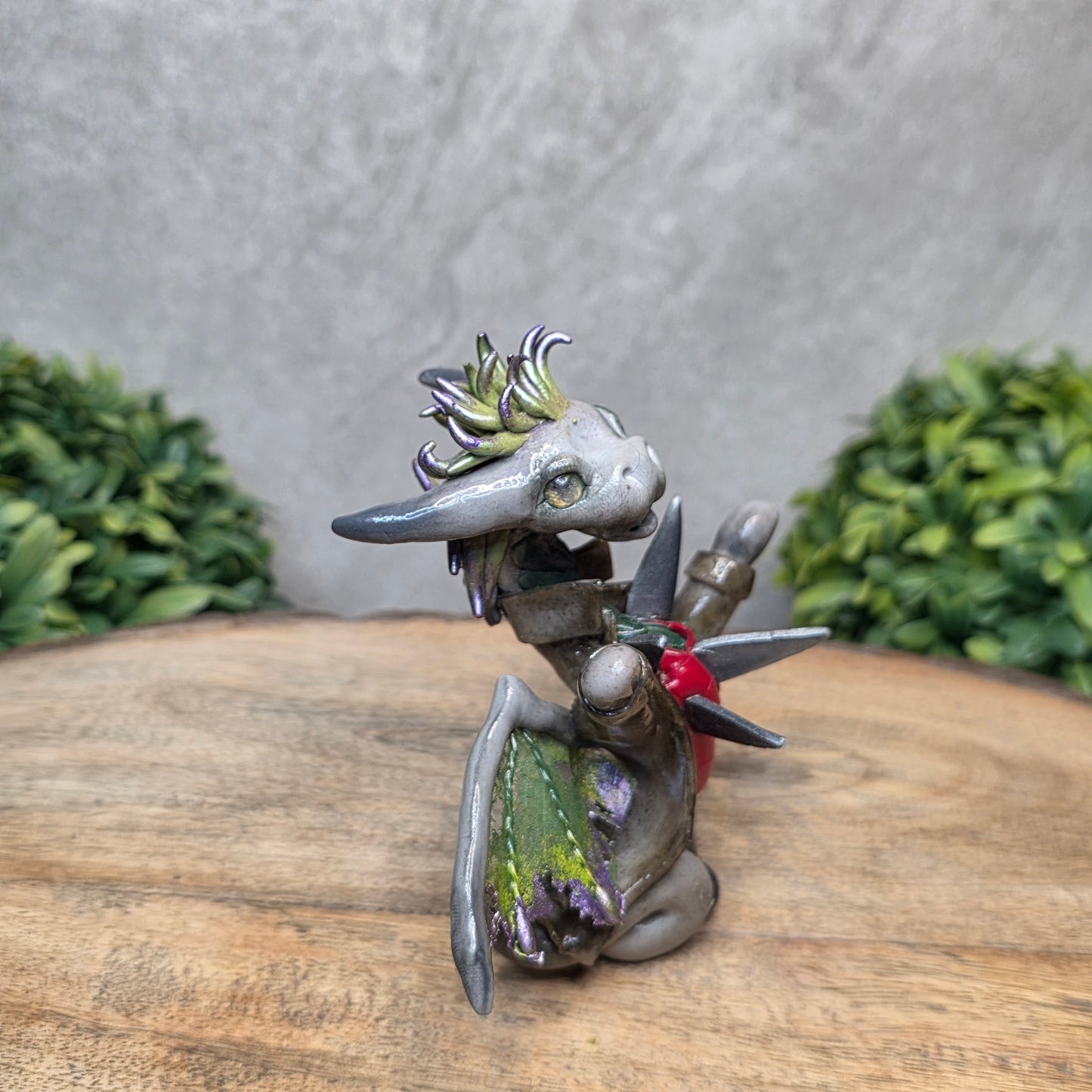 Clay dragon in costume on a wood surface with greenery.