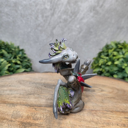Clay dragon in costume on a wood surface with greenery.
