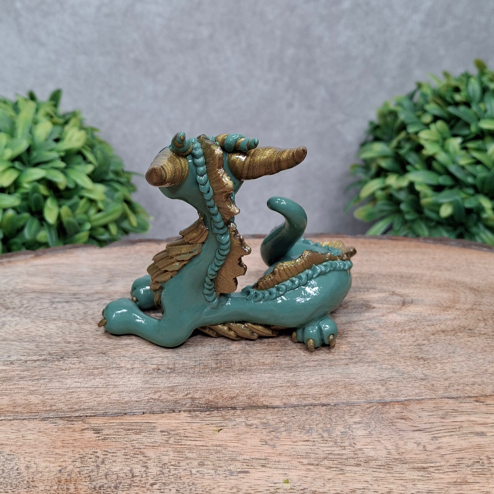 A clay dragon against a wood background with greenery