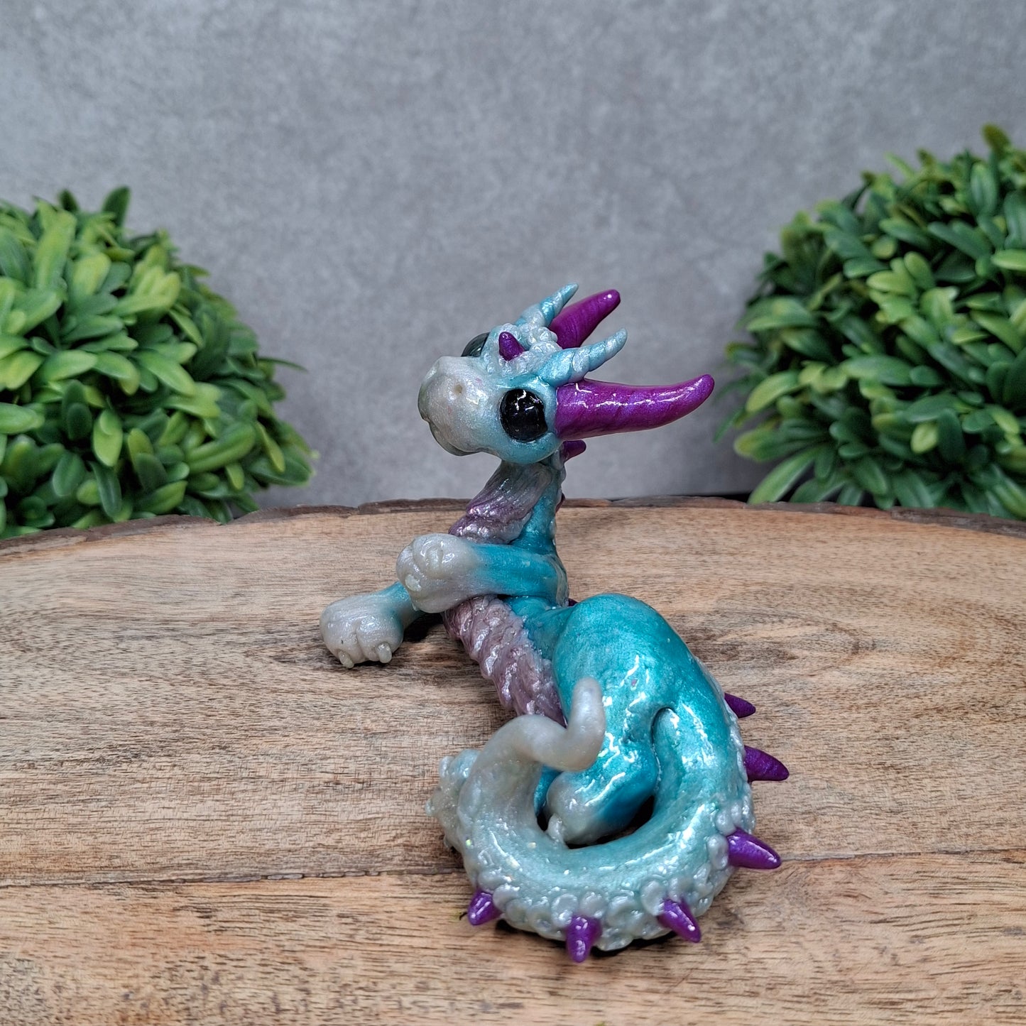A clay dragon against a wood background with greenery