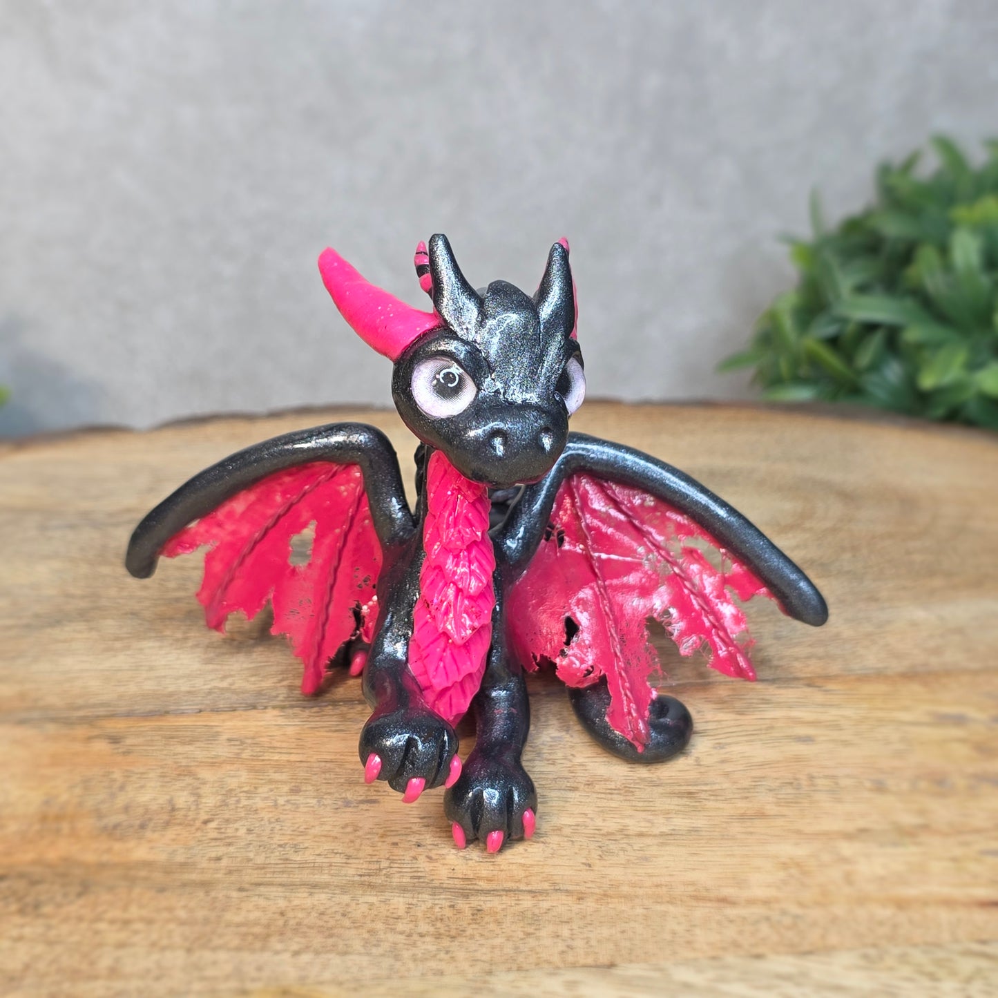 A graphite and pink clay dragon against a blurred wood surface