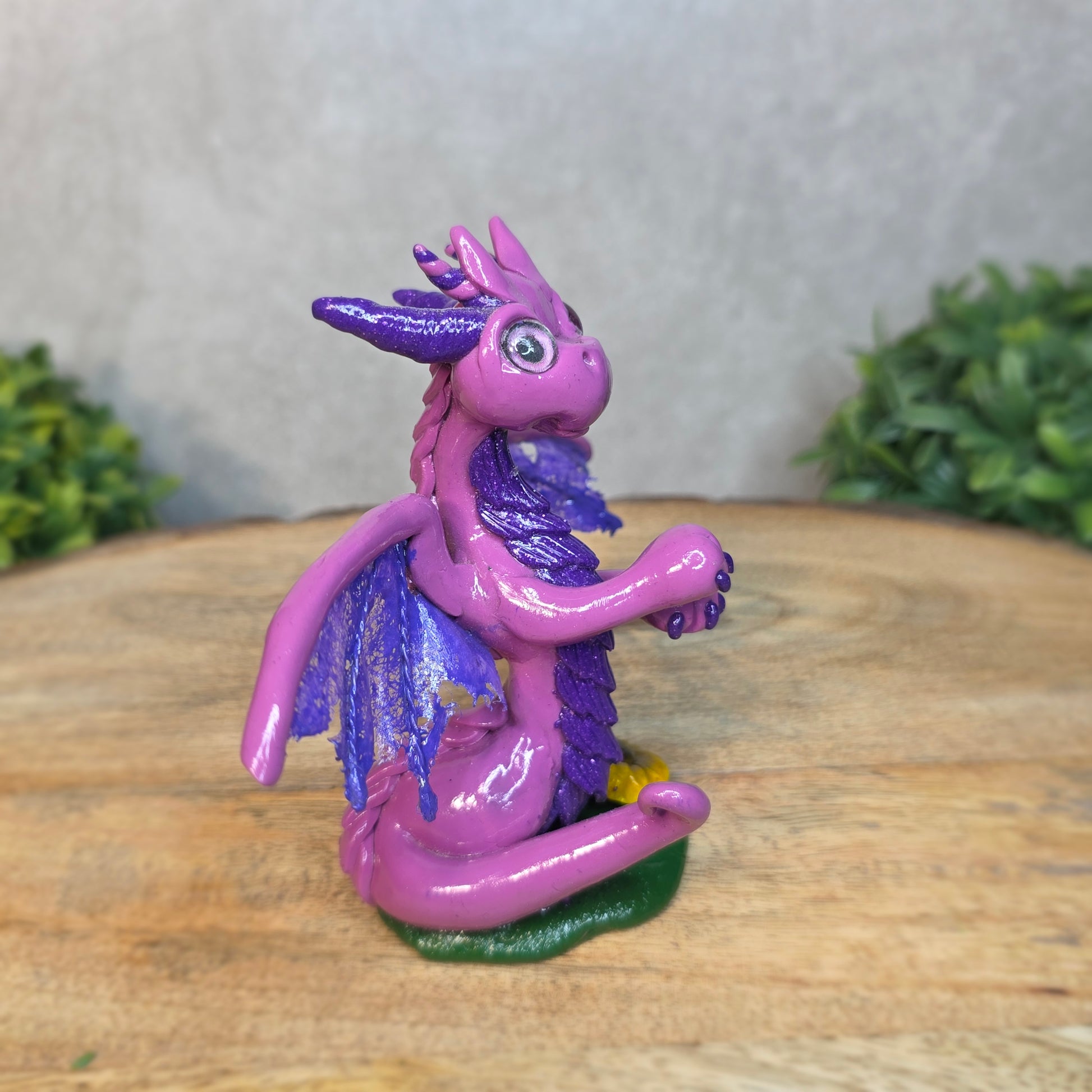 A clay dragon figurine on a wooden surface with a blurred green plant in the background