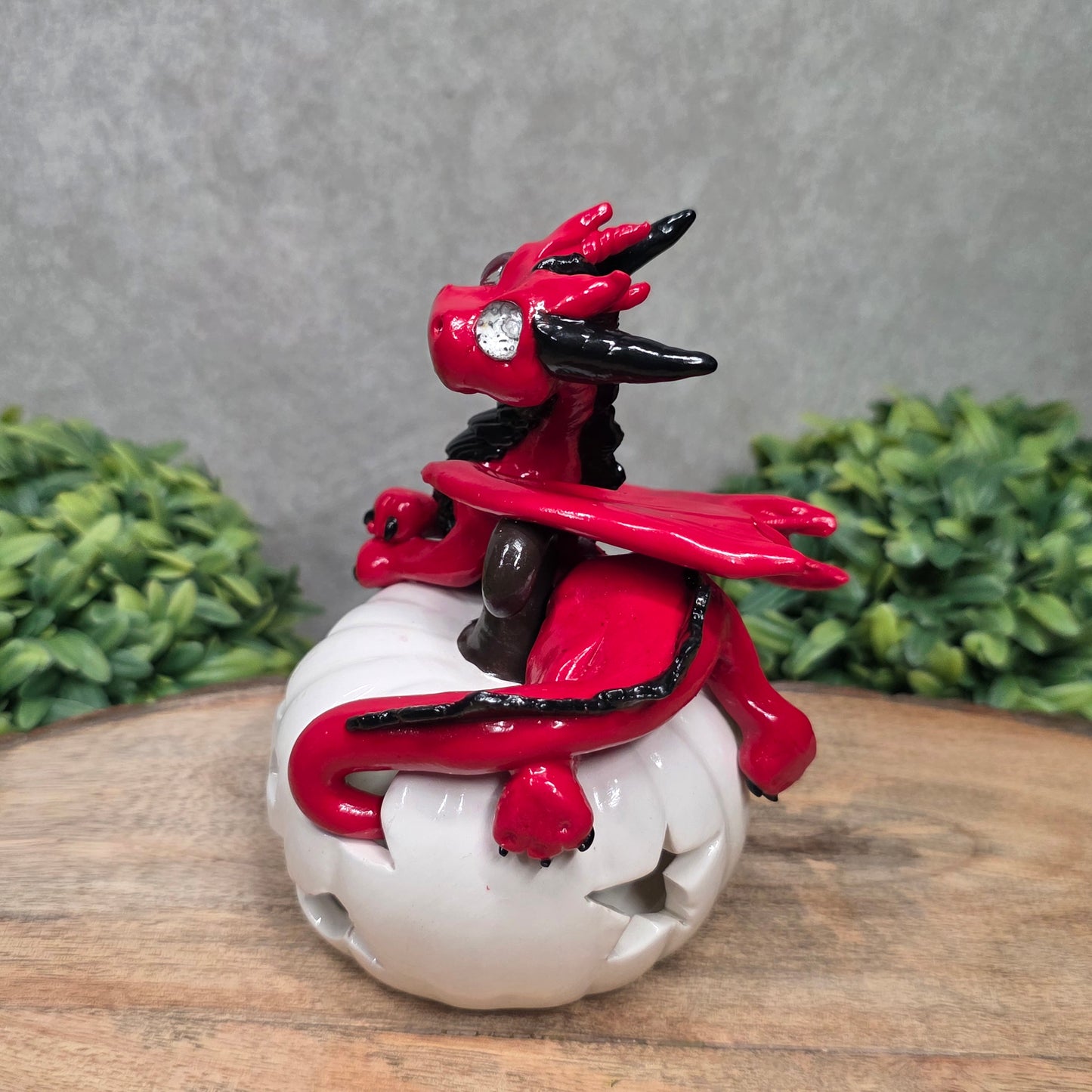 A red dragon sculpture on a white jack o lantern with greenery