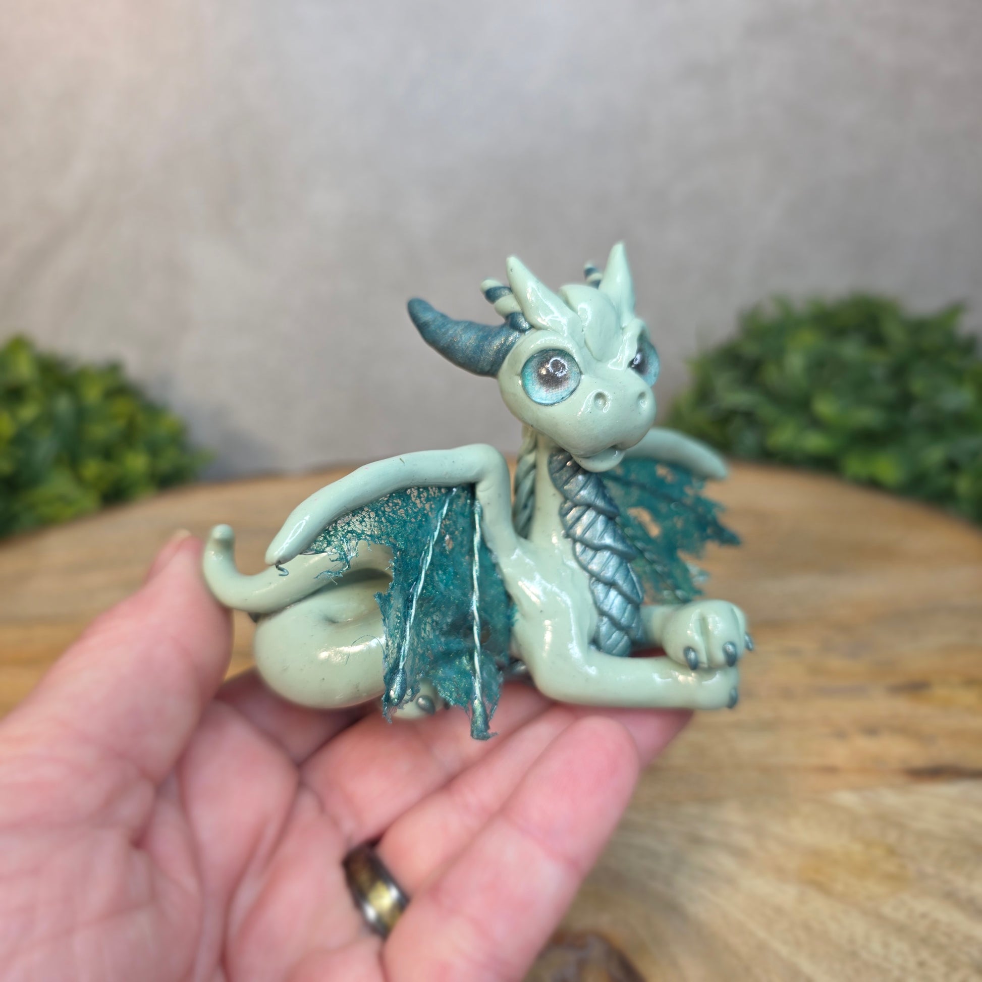 A hand holding an aqua and turquoise clay dragon against a blurred wood surface