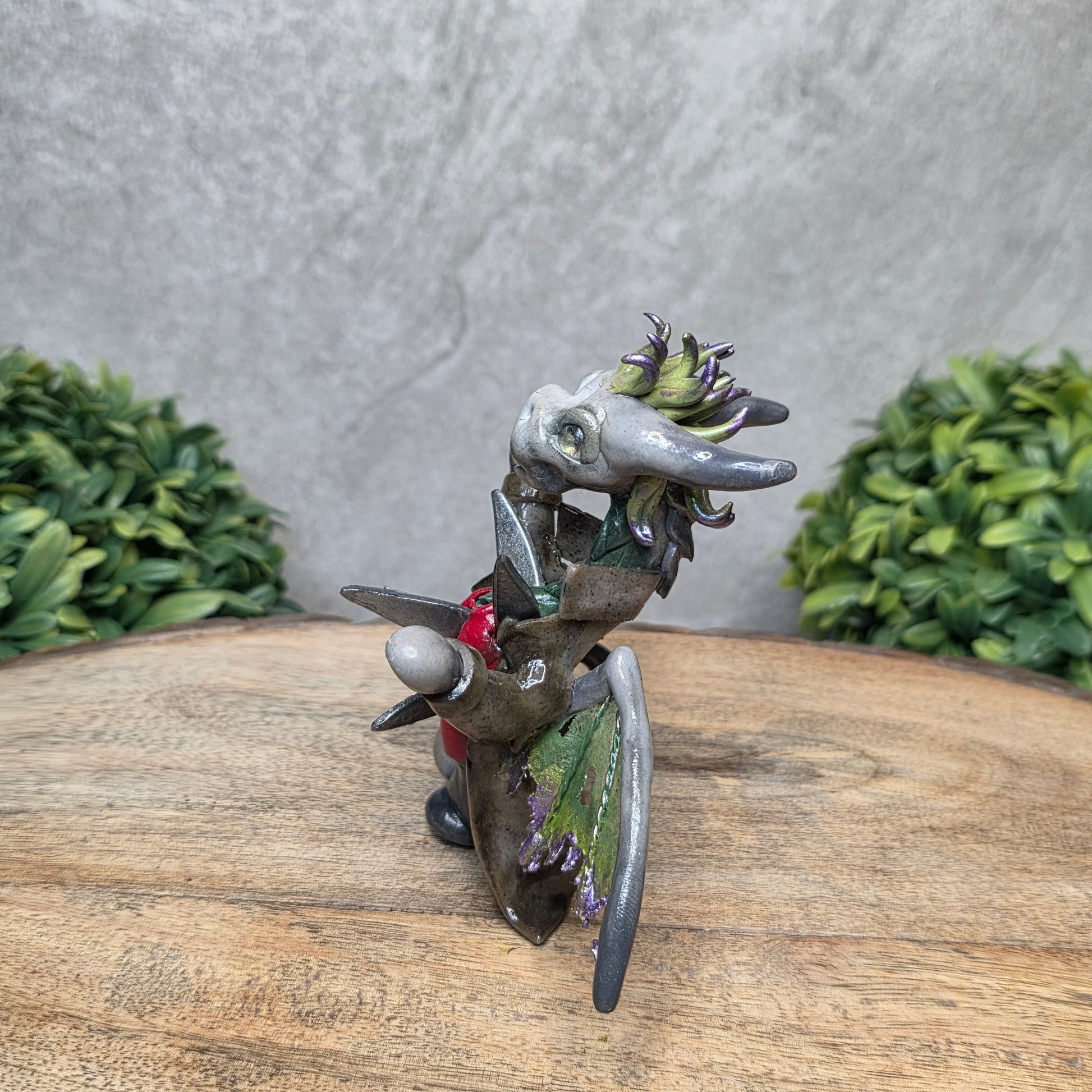 Clay dragon in costume on a wood surface with greenery.