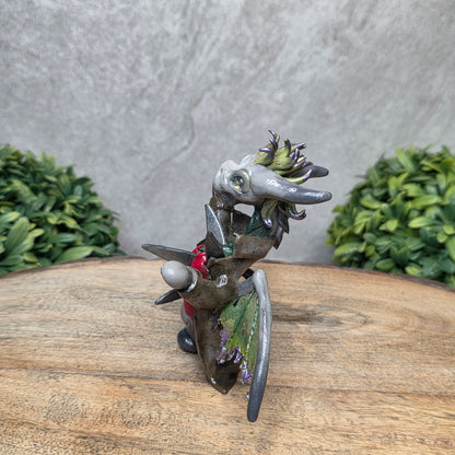 Clay dragon in costume on a wood surface with greenery.